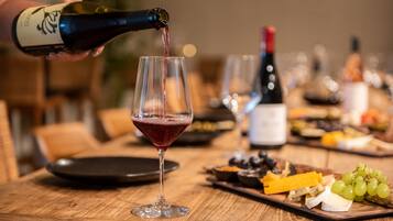 A wine bottle being poured into a glass, a cheese board with various cheeses and grapes, and a bottle of red wine in the background.