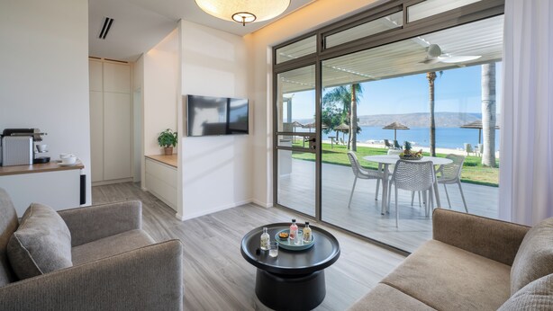 A modern living room with a large sliding glass door leading to an outdoor patio with a view of the beach. - Ein Gev Holiday Resort (Emek HaYarden)