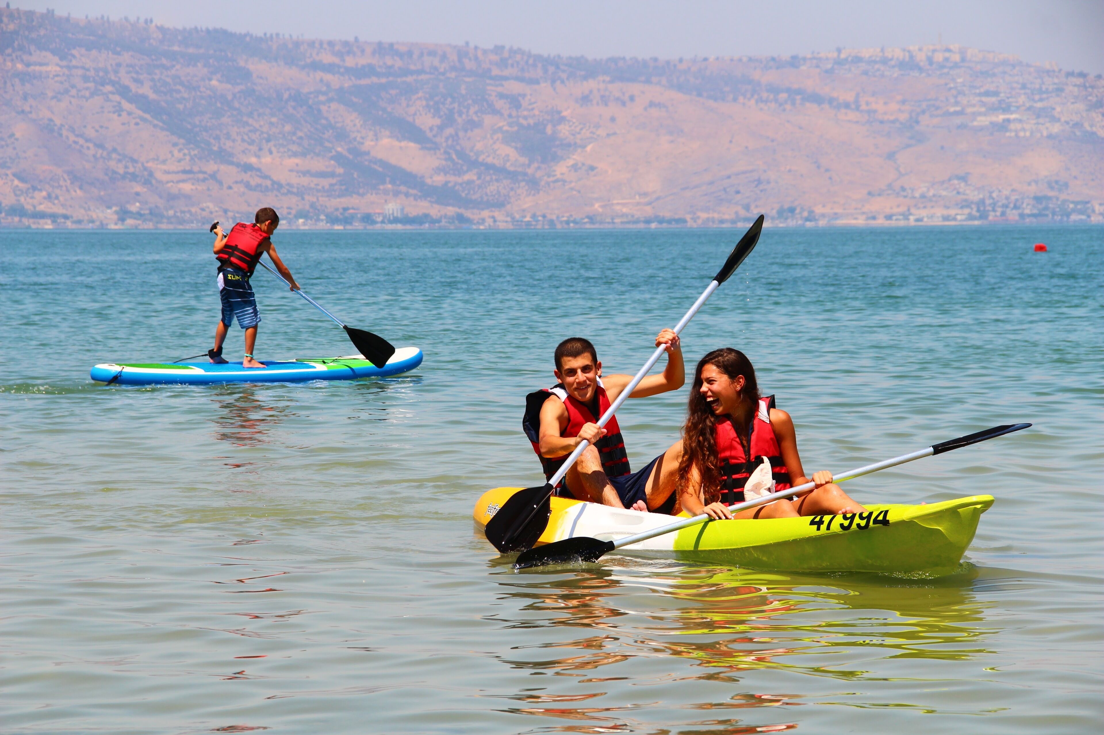 Un grupo de personas haciendo kayak en un lago tranquilo con colinas al fondo.