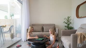 Deux enfants jouent à un jeu de société autour d’une table ronde dans un salon, où se trouvent un canapé et une plante en pot.