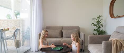 Dos niños jugando un juego de mesa en una mesa redonda en una sala de estar con un sofá y una planta en maceta.
