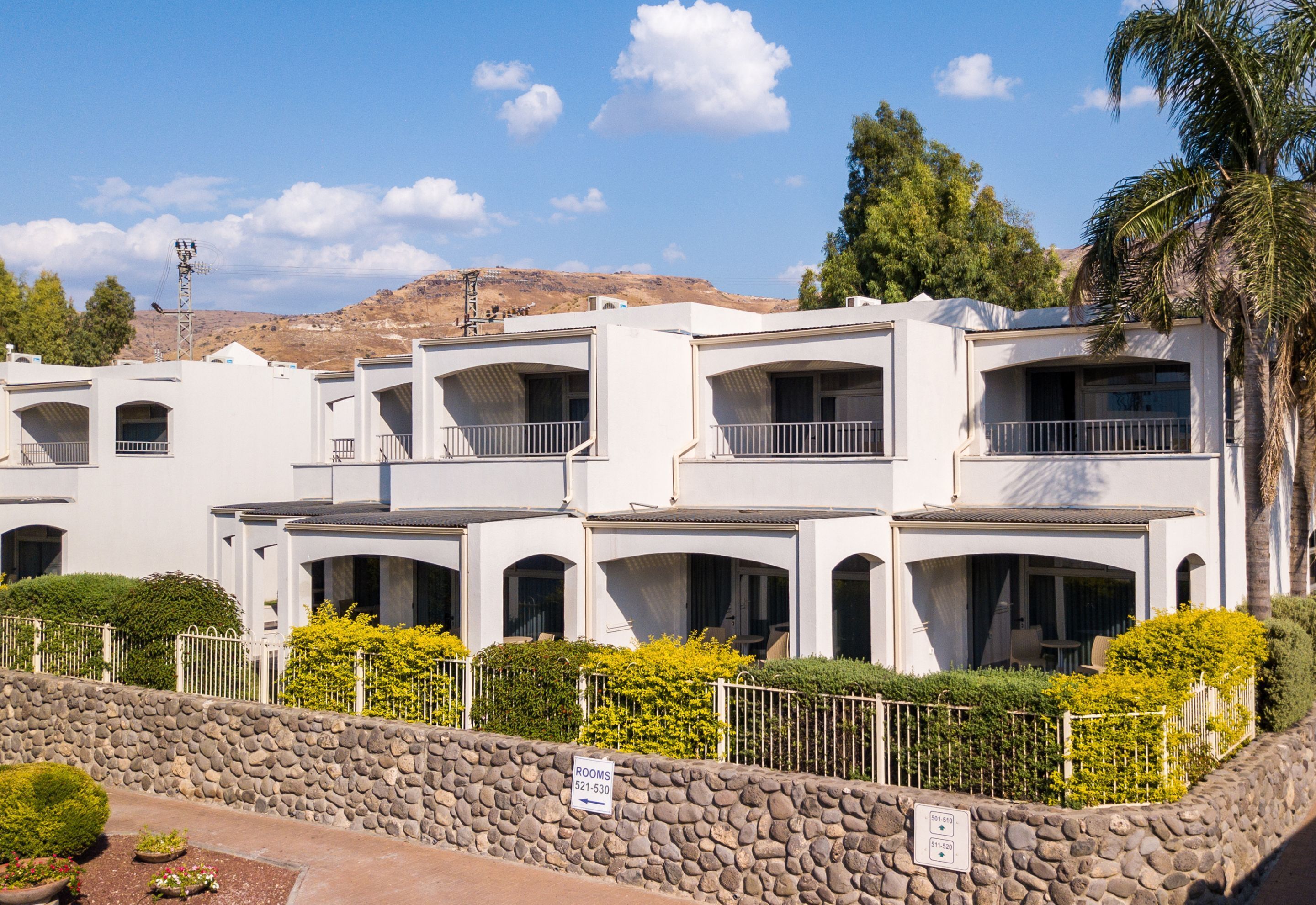 Una hilera de edificios blancos de varios pisos, con balcones, un muro de piedra y un letrero que indica las habitaciones 521-530.