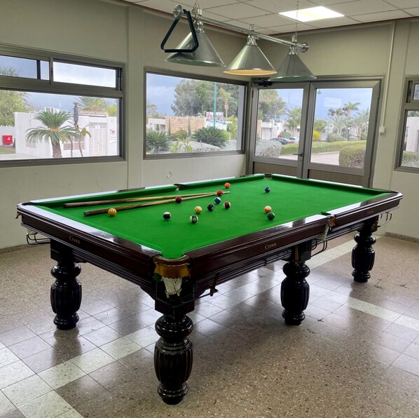 A pool table with balls, a chandelier, and windows with a view of the outside.