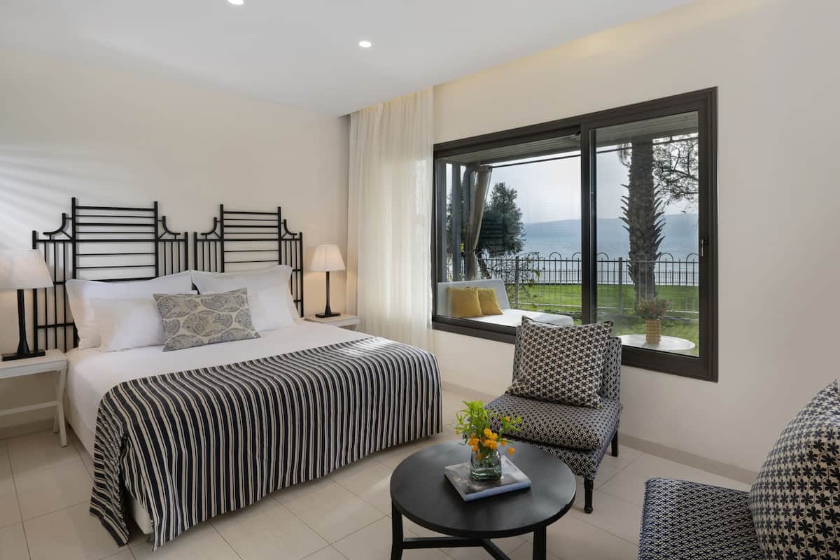 A bedroom with a large bed, a sofa, a small table, and a window with a view of the sea.