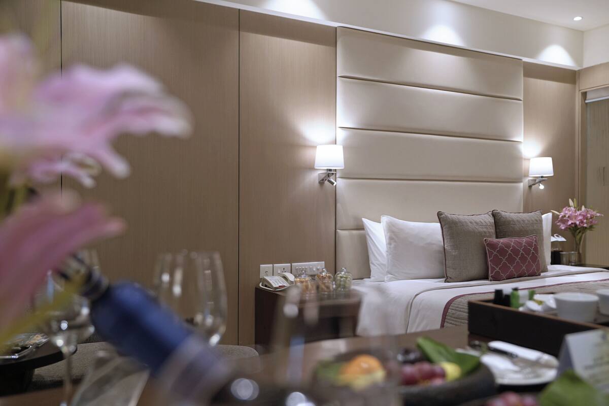 A hotel room with a bed, bedside lamps, a nightstand, and a dining area with a table set for two.