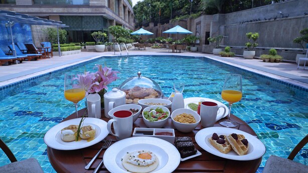 Ein Frühstücksbuffet am Pool mit verschiedenen Speisen, Getränken und einer Kaffeekanne.