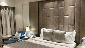 Ein modernes Hotelzimmer mit einem großen Bett, einem Beistelltisch, einem Sessel, einem Schreibtisch und einem Deckenventilator.