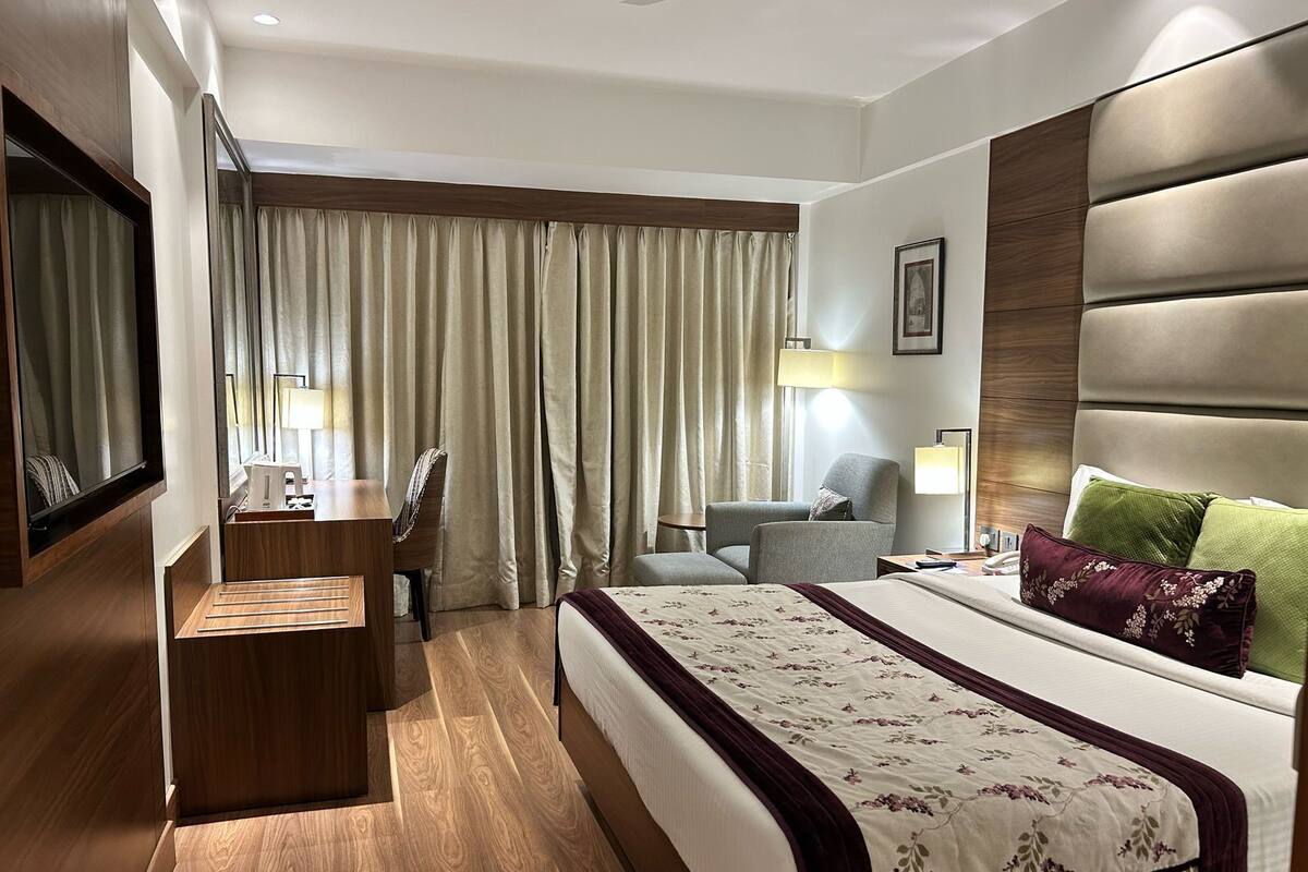 A hotel room with a bed, a desk, a chair, a lamp, and a window with curtains.