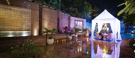 Un espace extérieur aménagé en terrasse, agrémenté d’un élément aquatique, de plantes en pot et d’un coin repas abrité sous une tente.