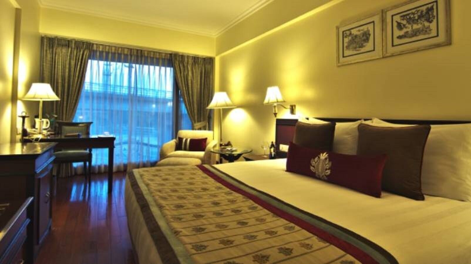 Ein Hotelzimmer mit einem großen Bett, zwei Nachttischen, einem Schreibtisch, einem Sessel und einem Fenster mit Vorhängen.