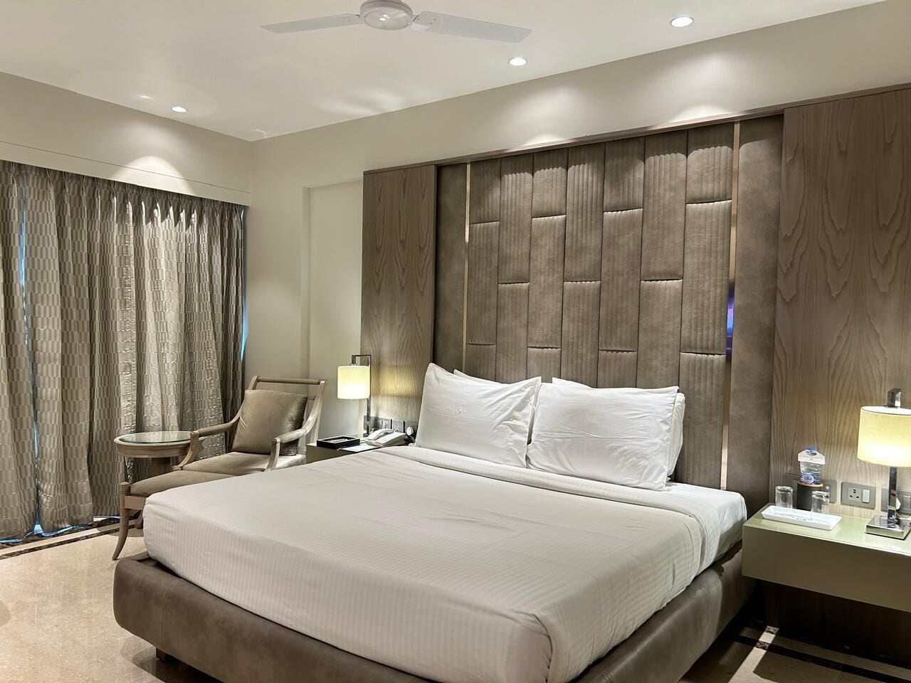 A hotel room with a large bed, a chair, a desk with a lamp, and a curtain.
