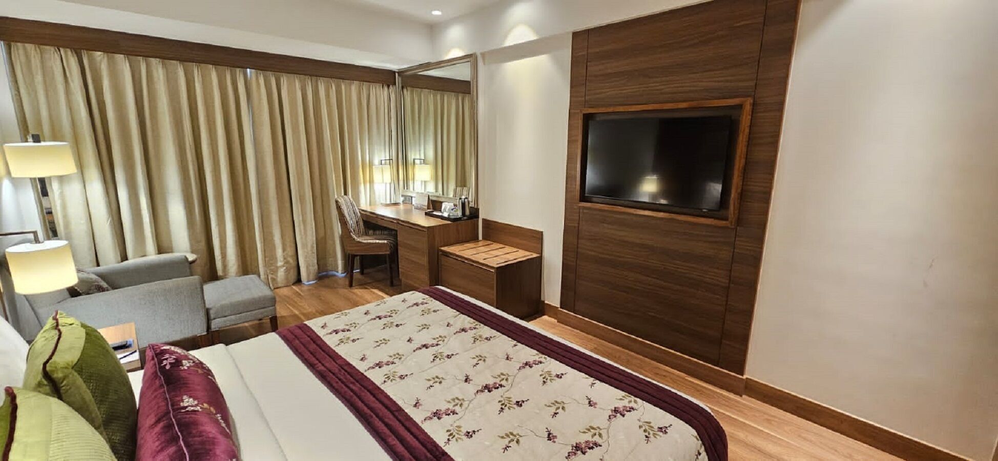 A hotel room with a bed, a desk, a chair, a TV, and curtains.