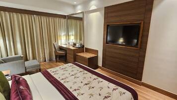 A hotel room with a bed, a desk, a chair, a TV, and curtains.