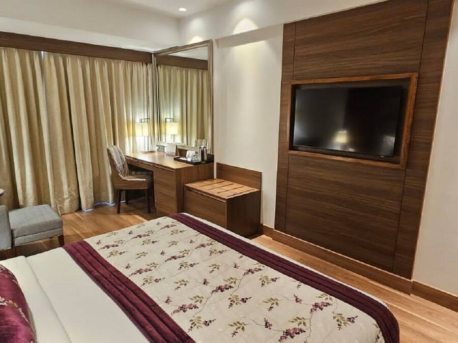 A hotel room with a bed, a desk, a chair, a TV, and curtains.