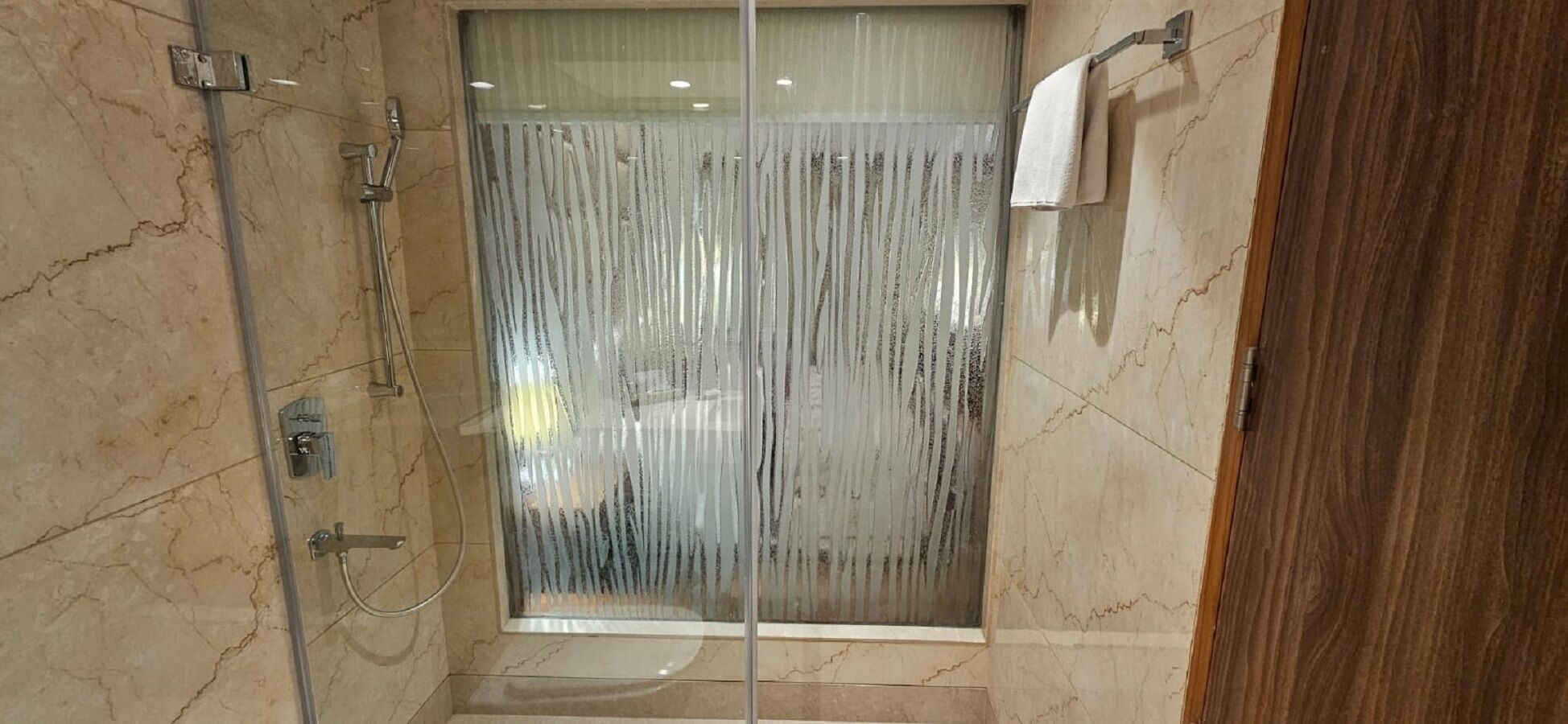 Un área de ducha con paredes de vidrio, suelo de mármol, un perchero y una puerta de vidrio.