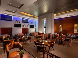 Un'ampia hall d'albergo con posti a sedere in pelle, una zona pranzo centrale e un palco con strumenti musicali.