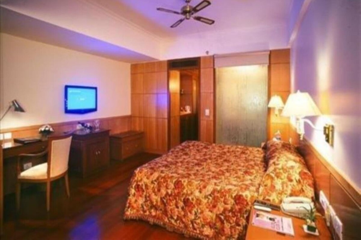 Una habitación de hotel con cama, escritorio, silla, televisor y ventilador de techo.
