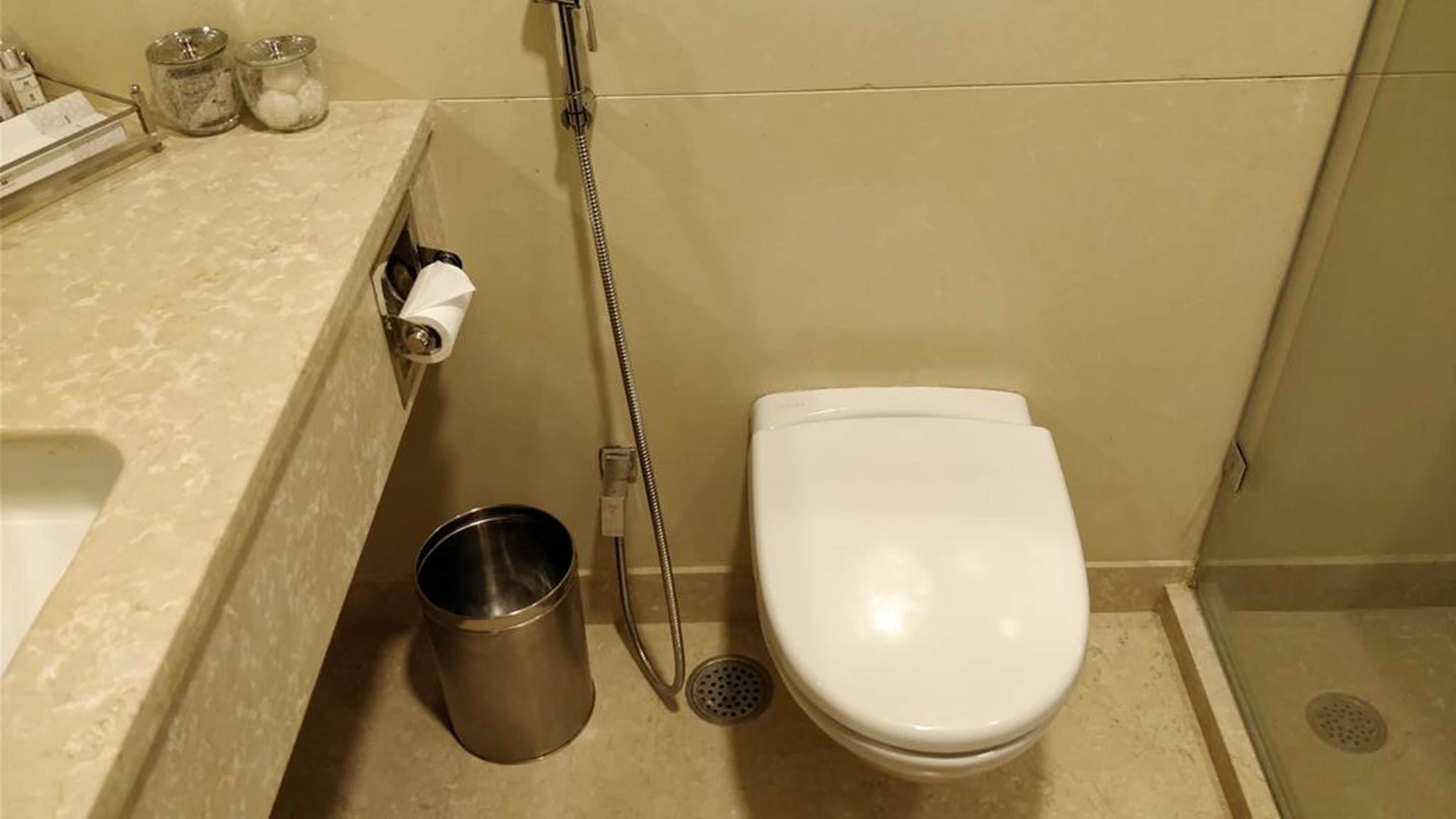 A bathroom with a white toilet, a shower, and a metal trash can.