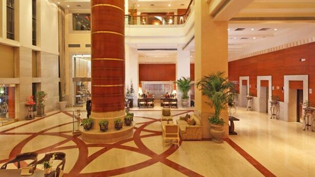 A spacious lobby with a central column, multiple seating areas, and a high ceiling with recessed lighting. - Jaypee Vasant Continental (New Delhi)
