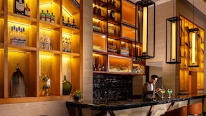 A bar area with shelves of bottles and glasses, a bar counter, and seating with a wooden table and chairs. - Jaypee Vasant Continental (New Delhi)