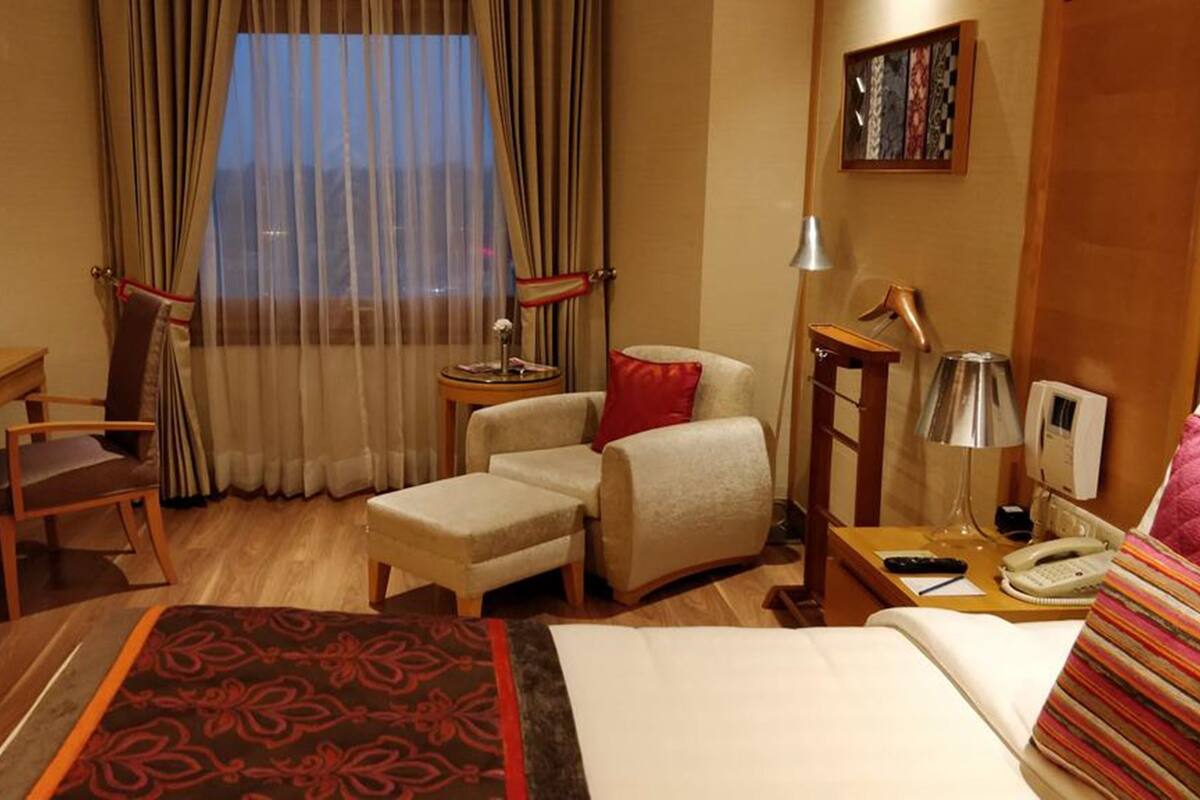 Habitación de hotel con cama, escritorio, silla, mesita y lámpara.