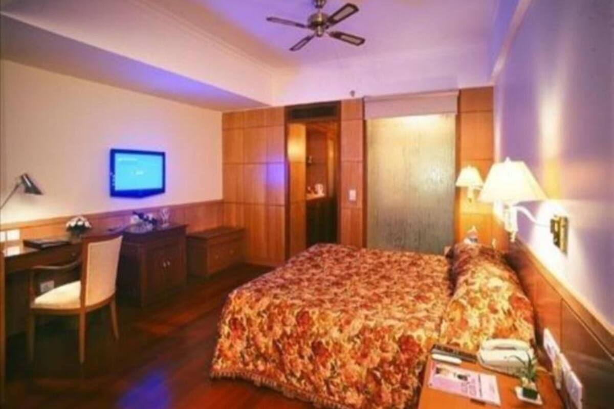 Una habitación de hotel con cama, escritorio, silla, televisor y ventilador de techo.