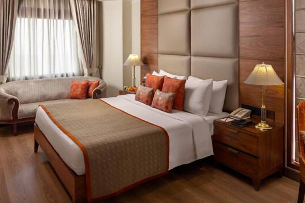 Habitación de hotel con cama, mesitas de noche, una silla, lámpara y ventana con cortinas.