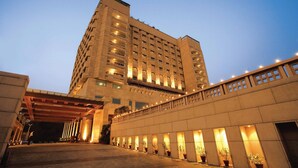 A multi-story hotel with a covered entrance and potted plants along the walkway. - Jaypee Vasant Continental (New Delhi)