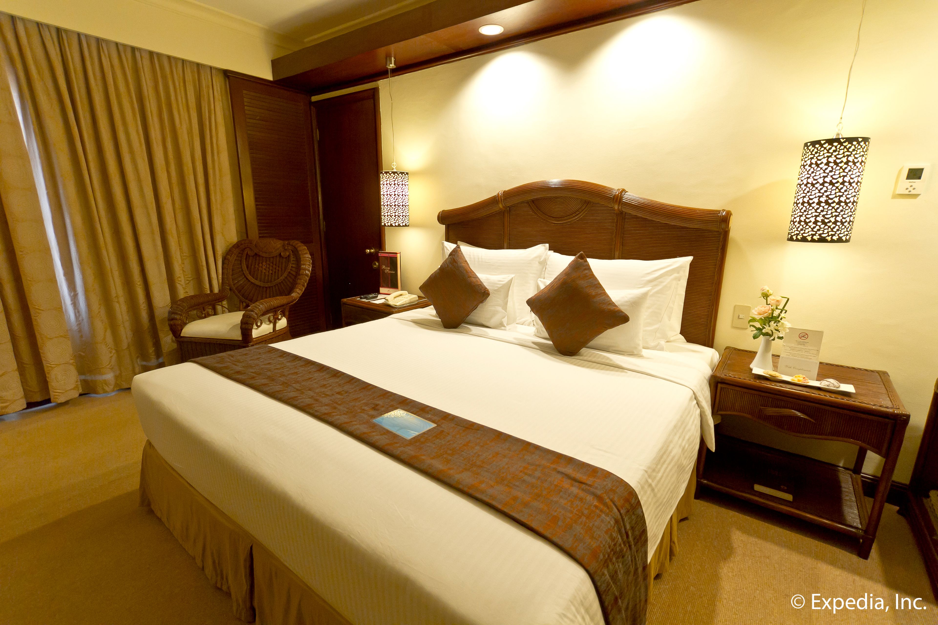 Ein Hotelzimmer mit einem großen Bett, einem hölzernen Kopfteil, einem Nachttisch, einem Sessel und einem Fenster mit Vorhängen.