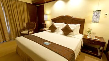 Ein Hotelzimmer mit einem großen Bett, einem hölzernen Kopfteil, einem Nachttisch, einem Sessel und einem Fenster mit Vorhängen.