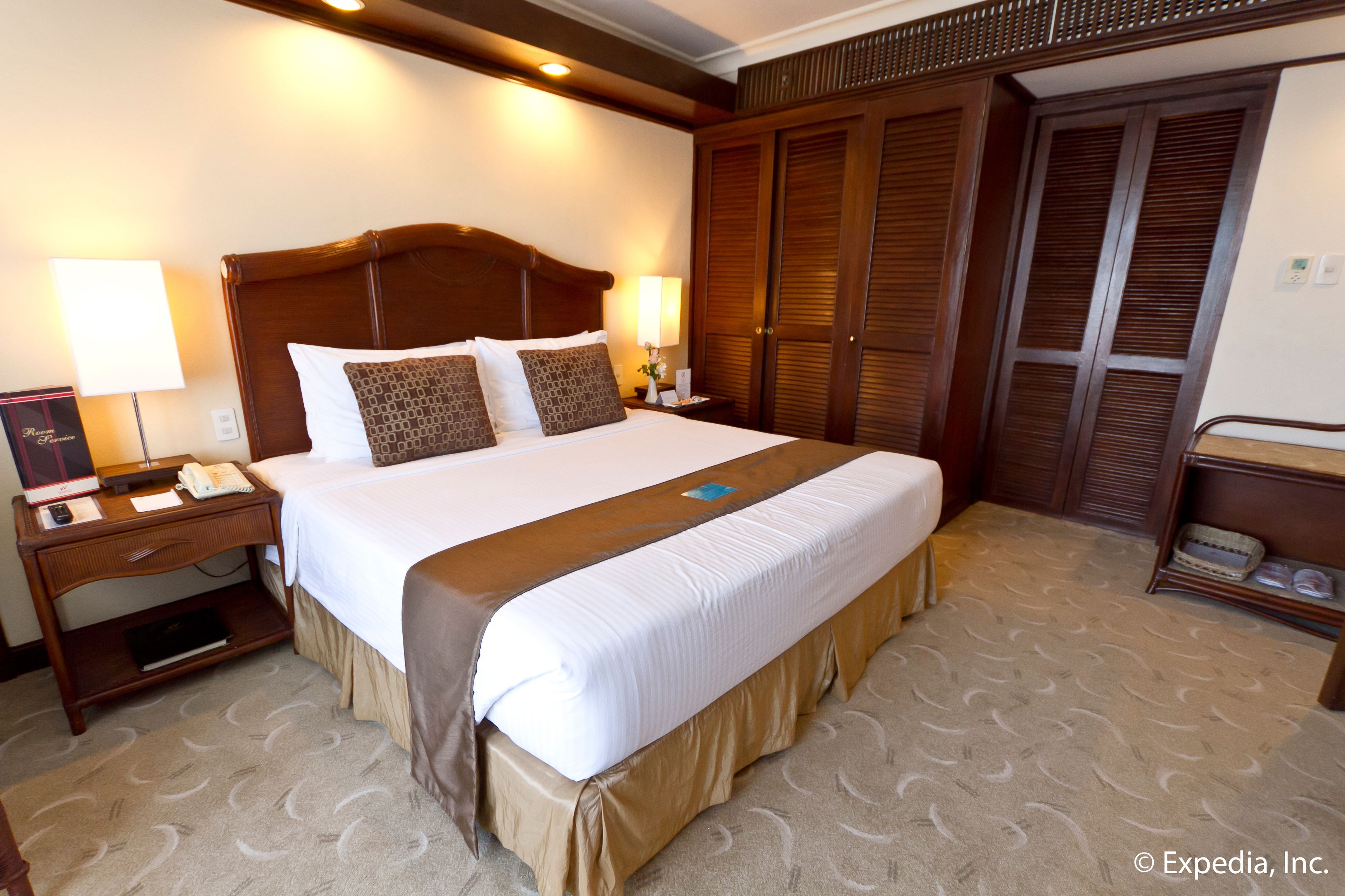 Een hotelkamer met een groot bed, een houten hoofdeinde, bedlampen, een nachtkastje, een bureau met telefoon en een garderobe met verstelbare deuren.