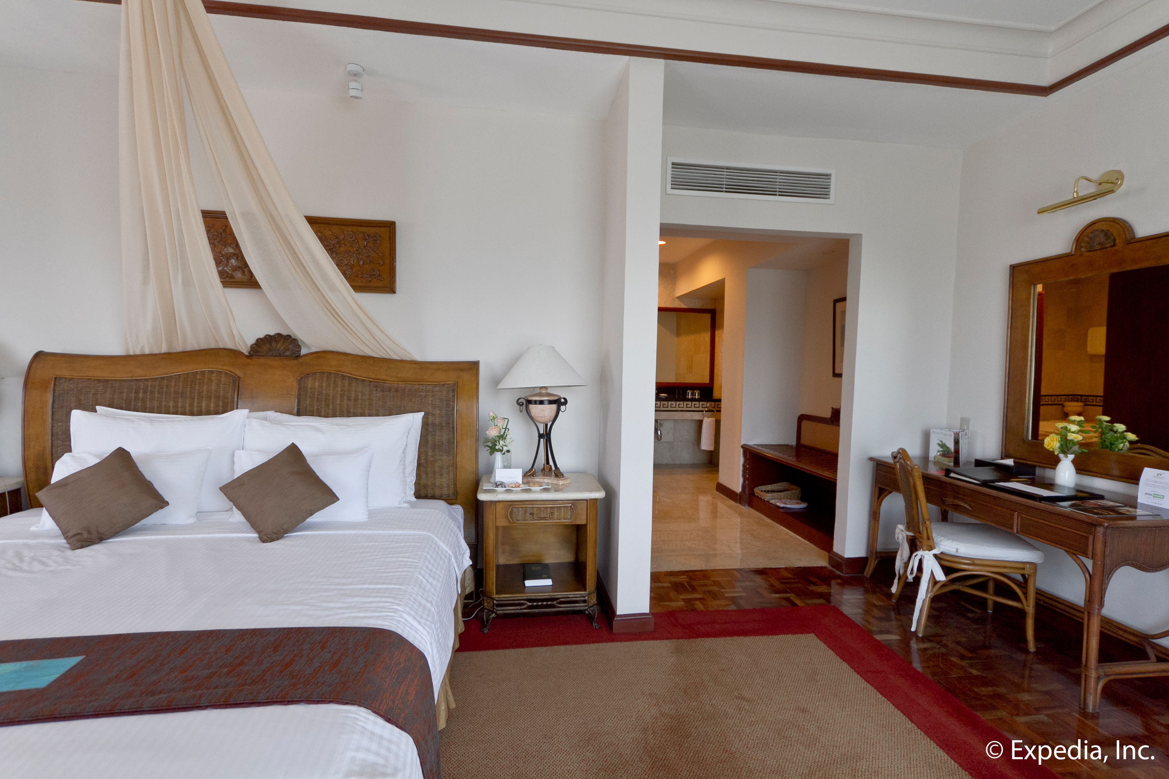 Habitación de hotel con una cama grande, un escritorio y una silla. Hay un espejo en la pared y una ventana con cortinas.