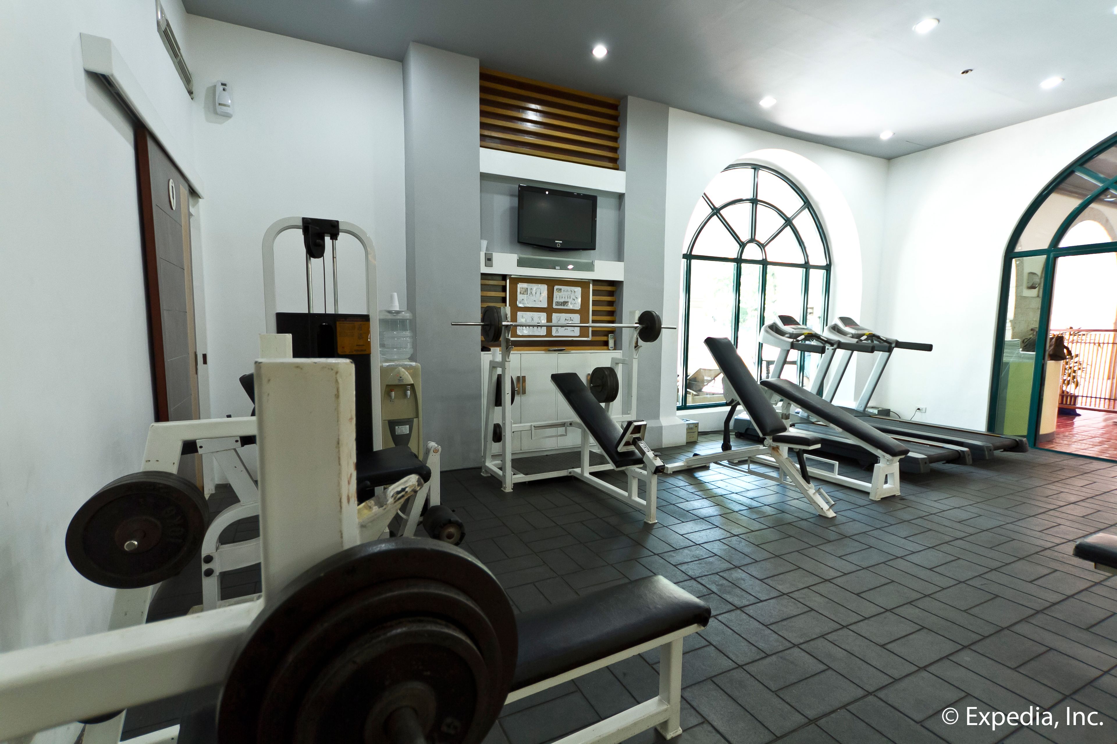 Un gimnasio con equipo de levantamiento de pesas, una televisión y máquinas de ejercicio.