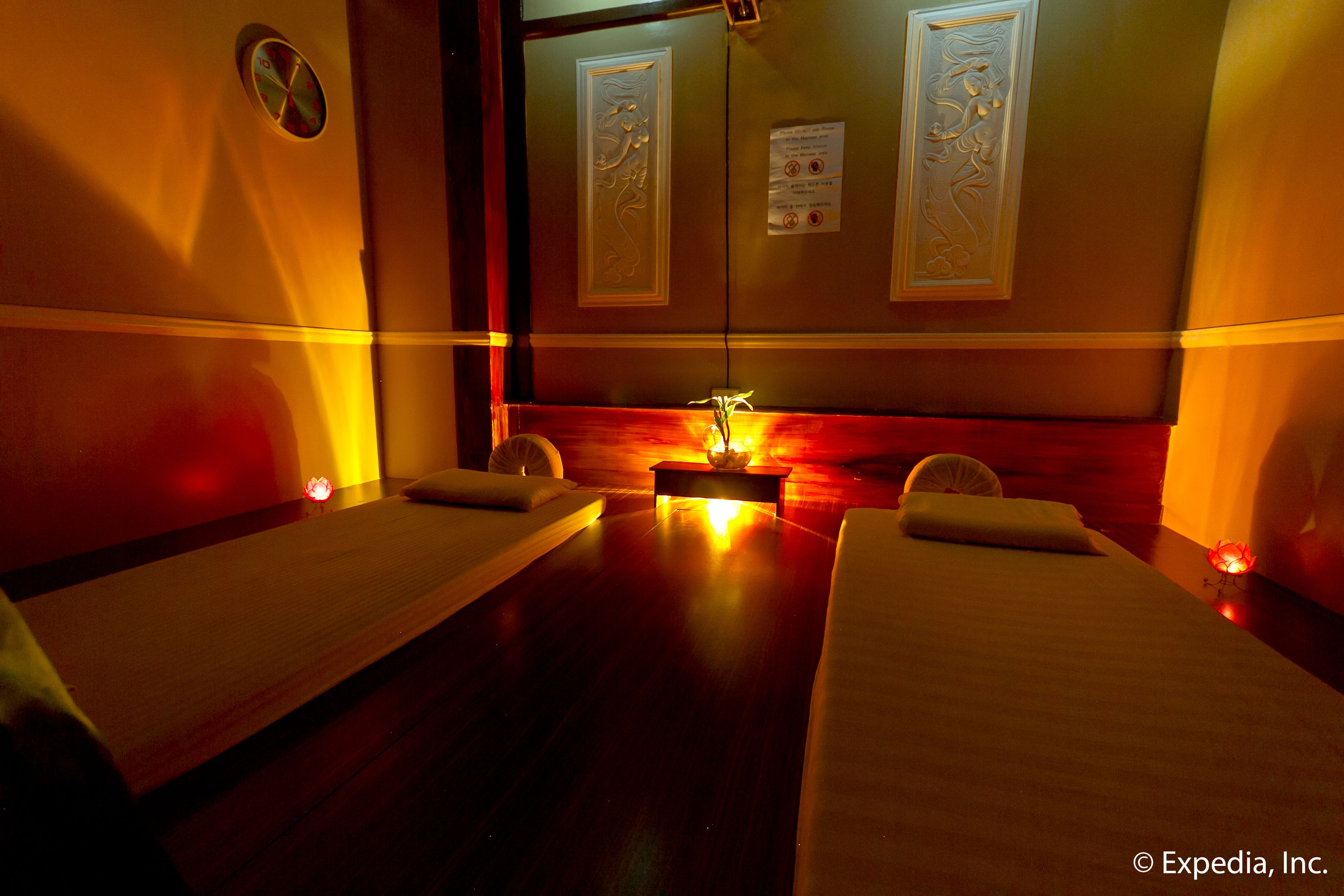 A room with two beds, a small table with a lamp, and a mirror with decorative panels.