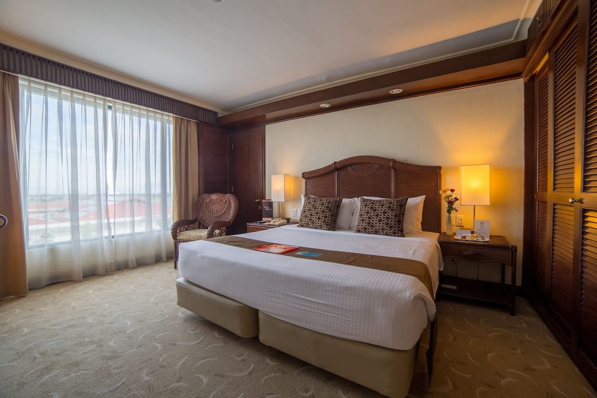 Una habitación de hotel con una cama grande, una mesita de noche, una lámpara y vistas al exterior.