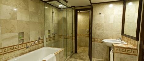 A bathroom with a bathtub, shower, and sink, all with marble tiles and a geometric border design.