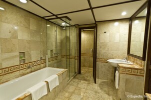A bathroom with a bathtub, shower, and sink, all with marble tiles and a geometric border design.