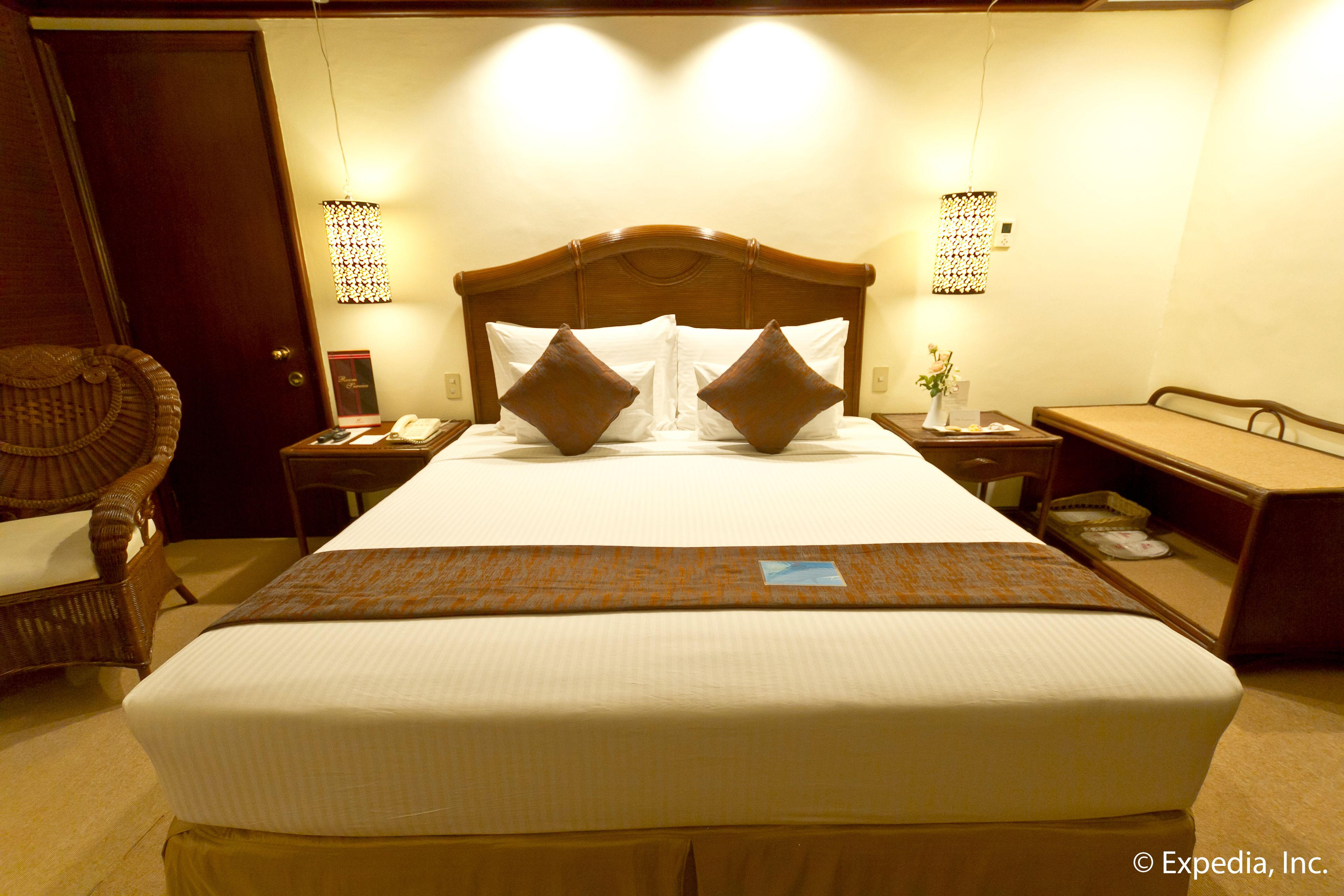 A hotel room with a large bed, two bedside tables, a chair, and a desk with a lamp.