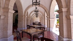 A dining area with stone arches, a chandelier, and tables and chairs.