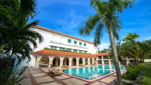 A hotel with a swimming pool, palm trees, and a courtyard with lounge chairs.