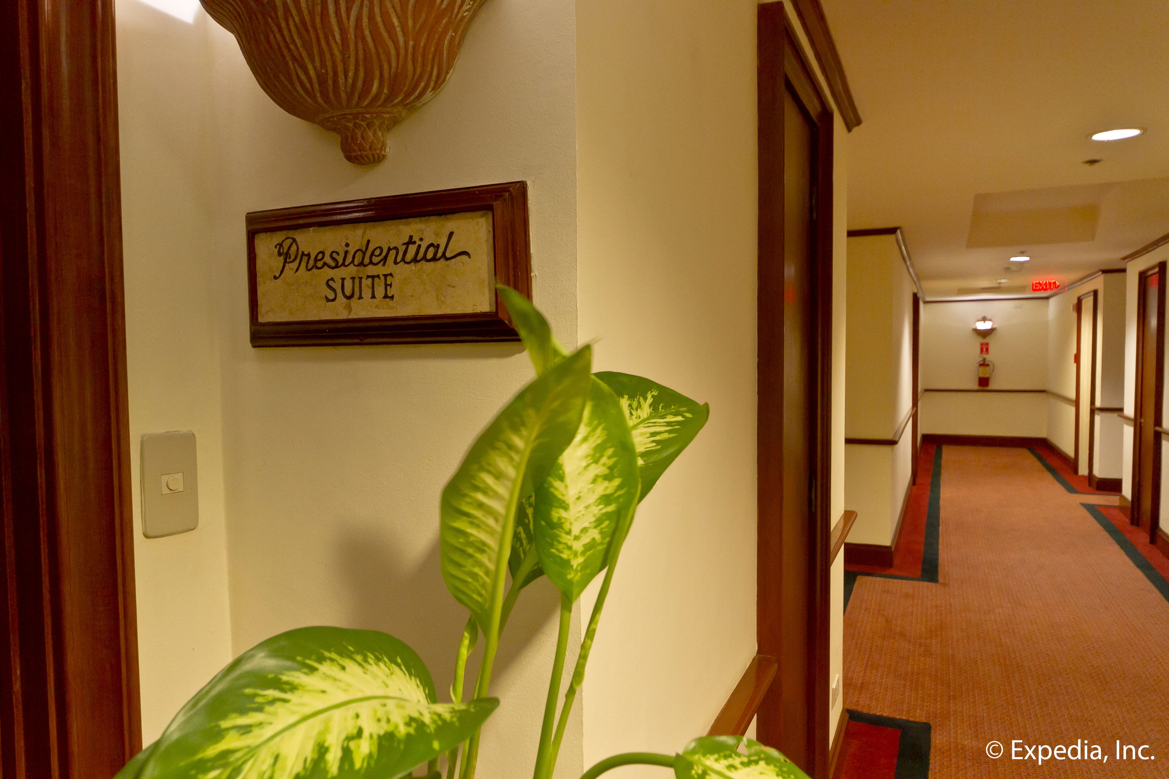A hallway with a sign reading "Presidential Suite," a wall-mounted light fixture, and a plant.