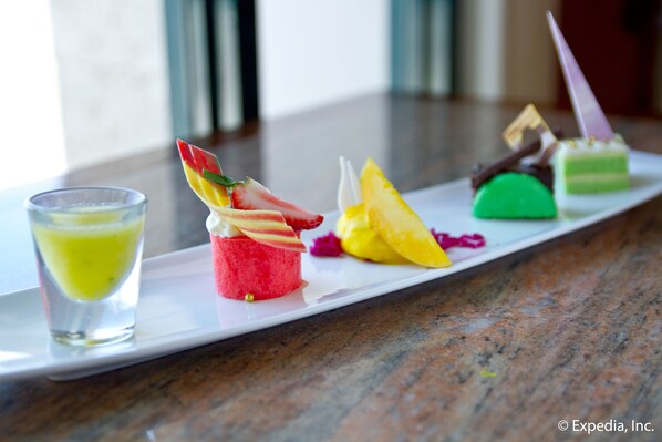 A dessert platter with various colorful treats and a glass of yellow beverage on a white plate.
