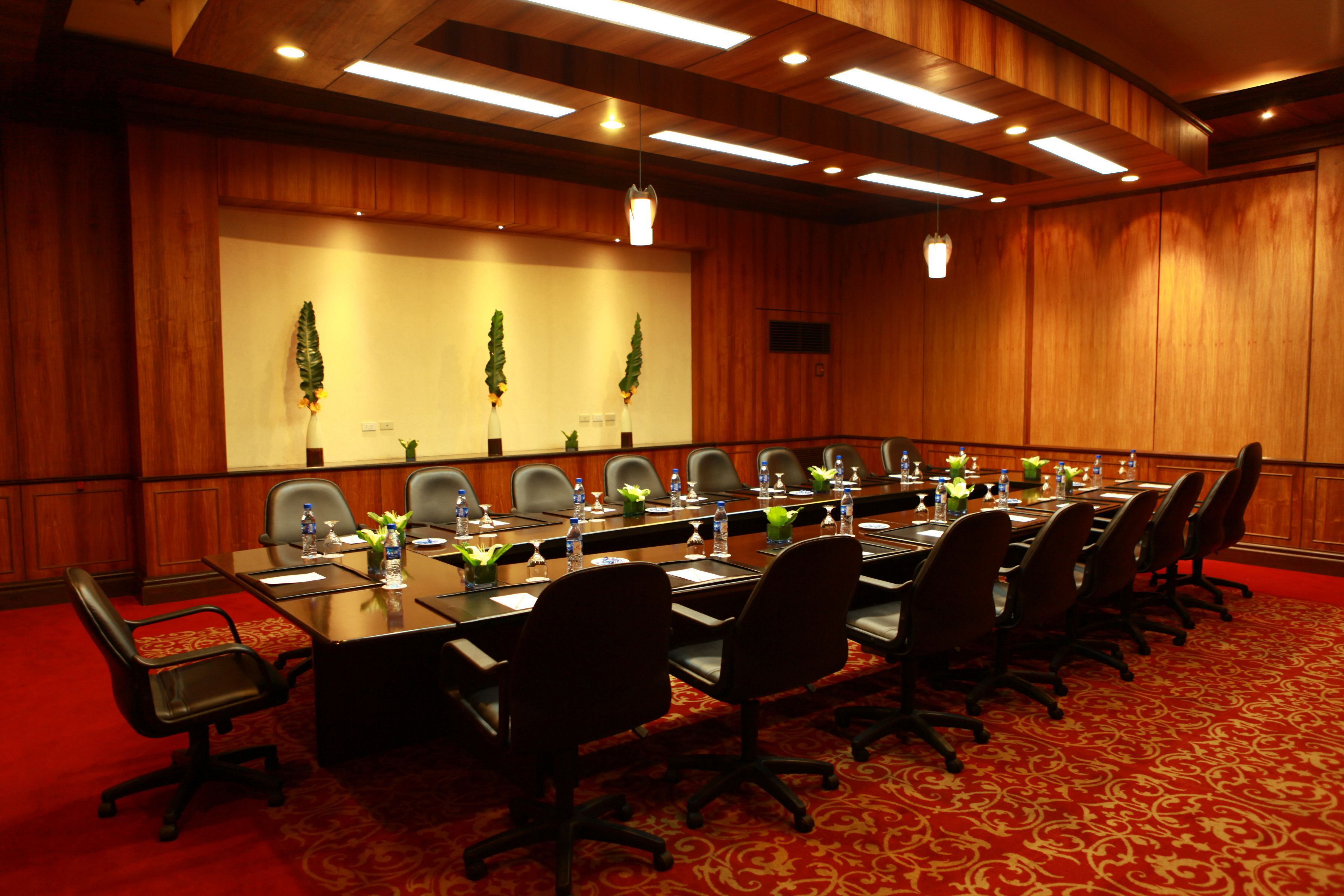 A conference room with a long table, multiple chairs, and a red carpeted floor.