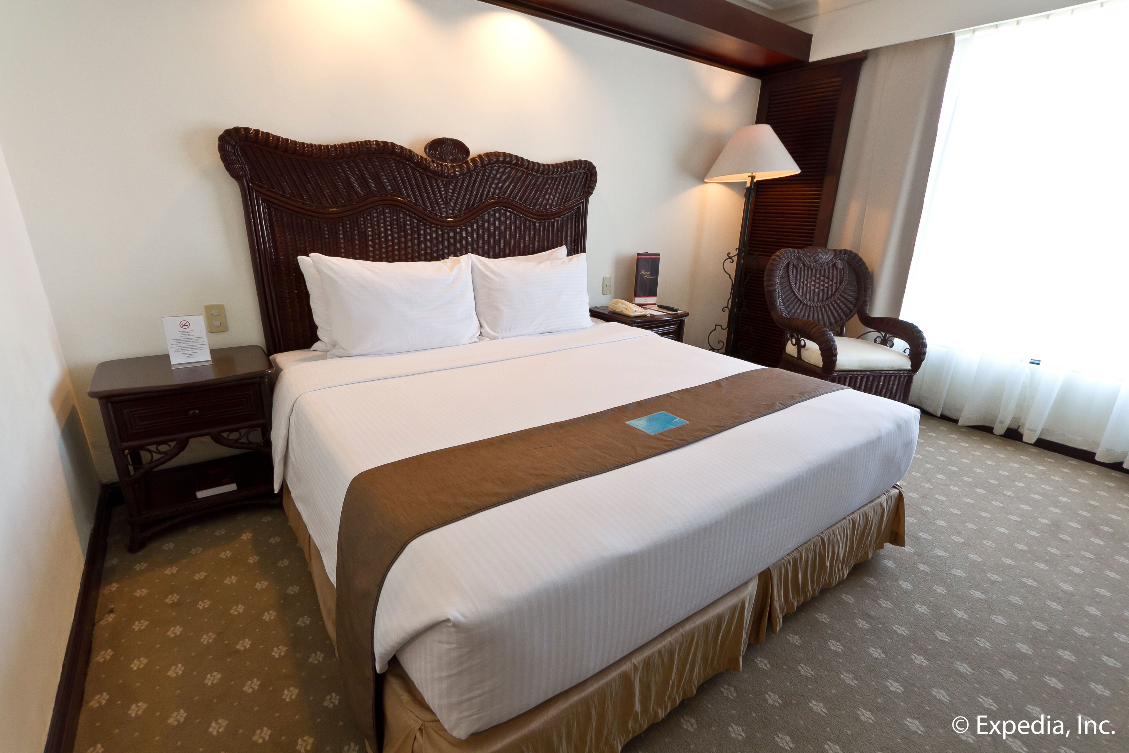 A hotel room with a large bed, a wooden headboard, a nightstand, a chair, and a lamp.
