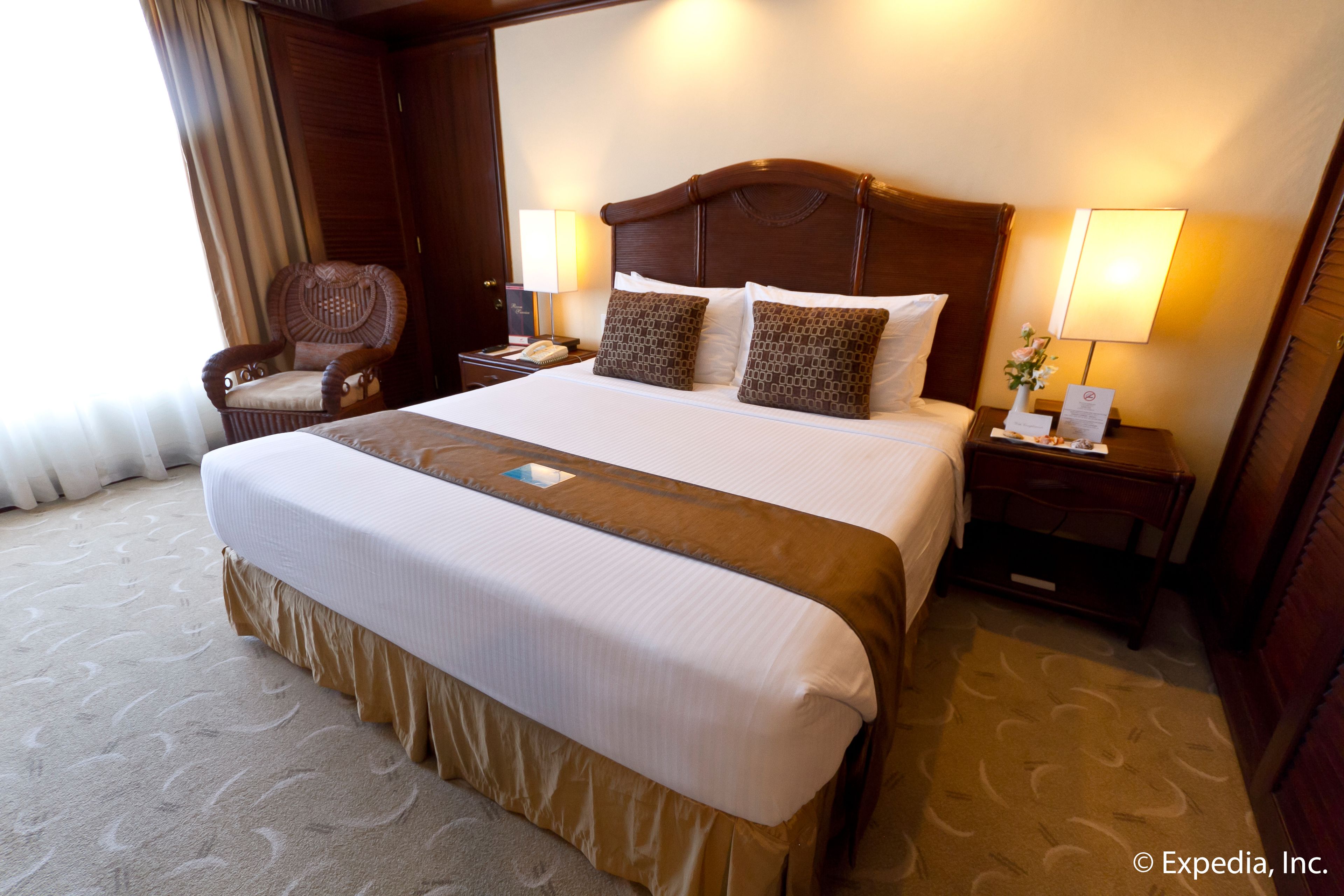 A large bed with a wooden headboard, two bedside tables with lamps, a chair, and a carpeted floor.