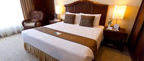 Una cama grande con cabecera de madera, dos mesitas de noche con lámparas, una silla y suelo cubierto de alfombra.