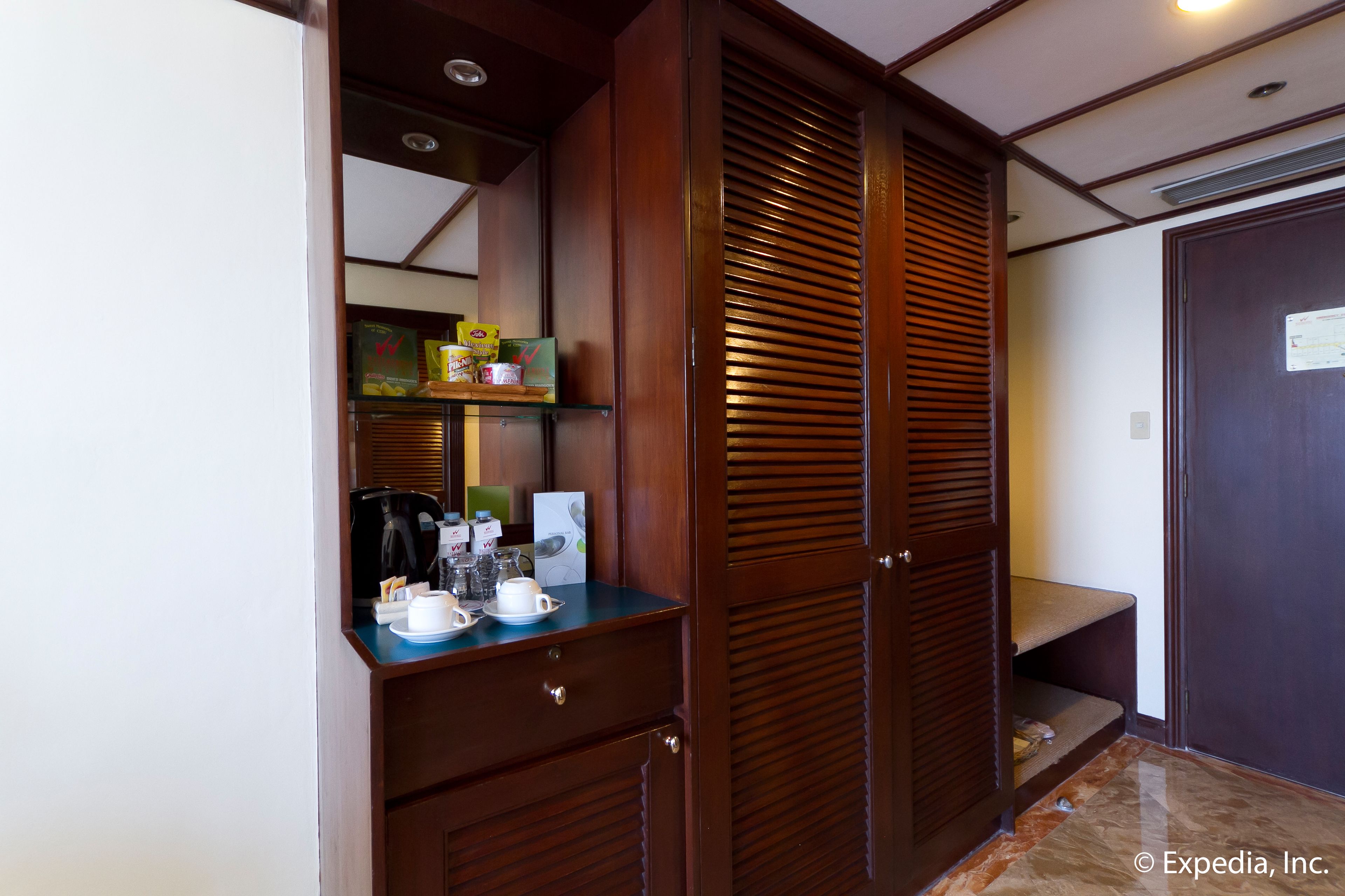 A wooden closet with a shelf containing a coffee maker, cups, and boxes.