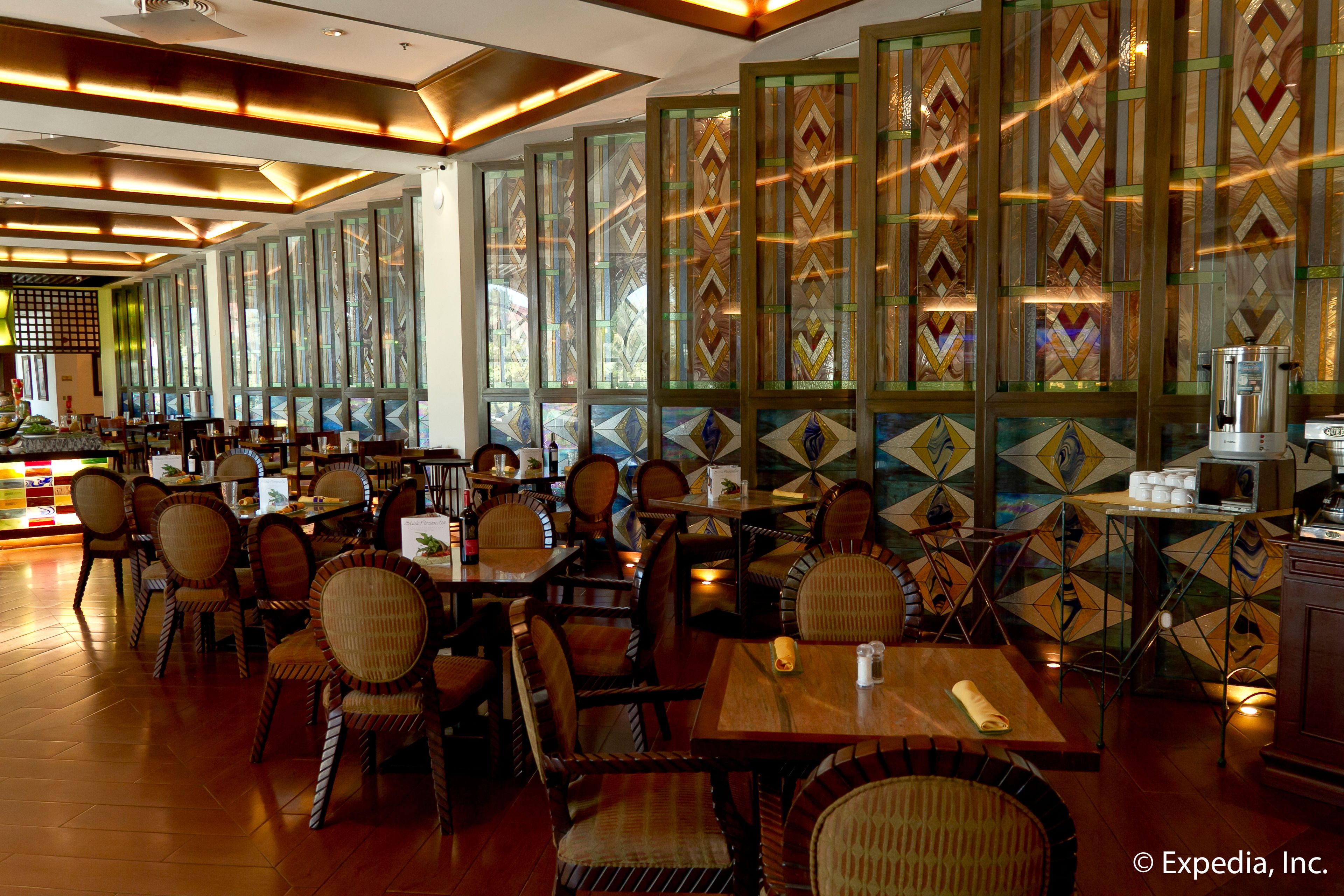A restaurant with wooden tables and chairs, large windows with geometric patterns, and a coffee machine on a counter.