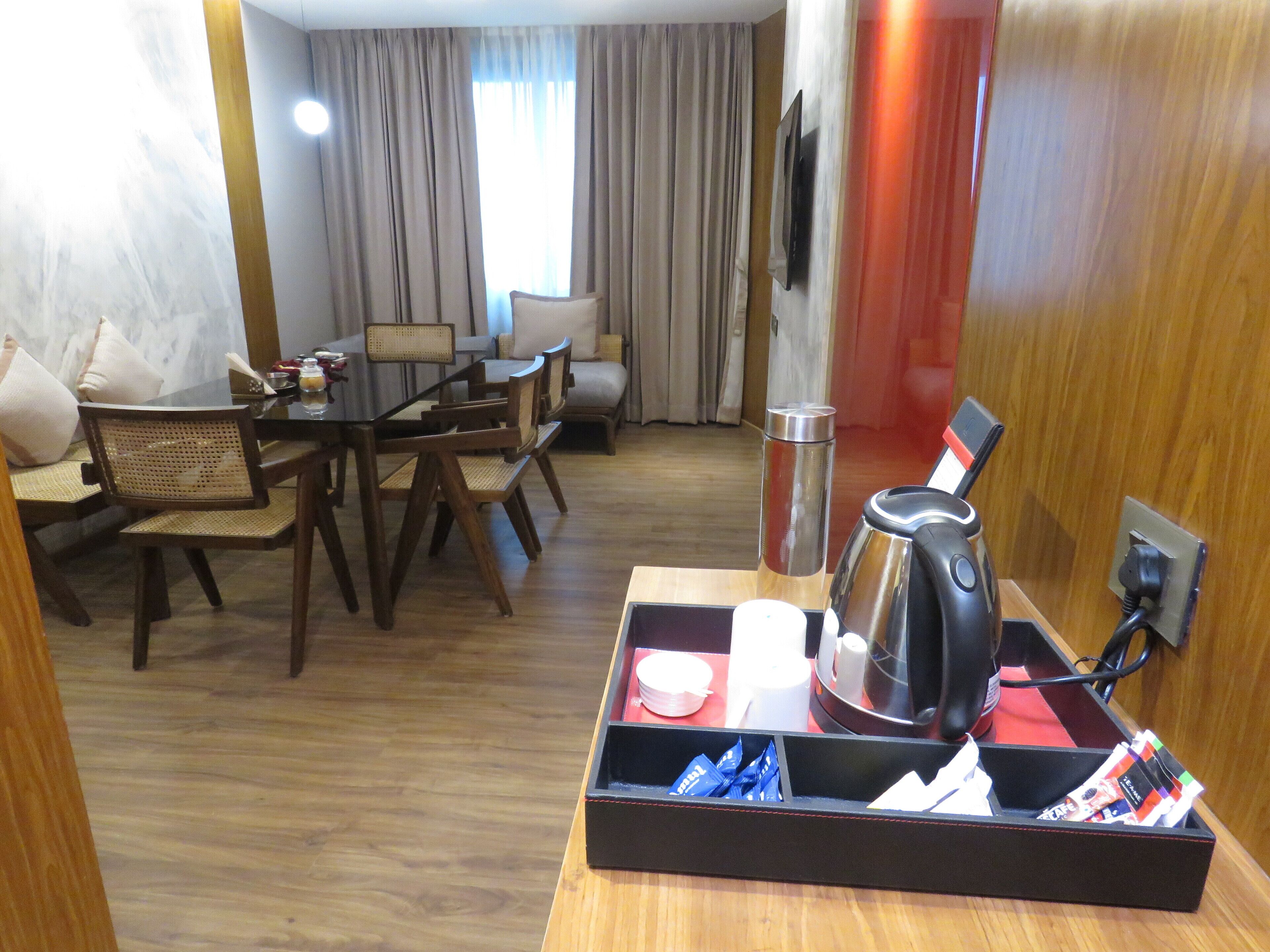 A hotel room with a dining area, a coffee maker, a tray with snacks, and a TV mounted on the wall.