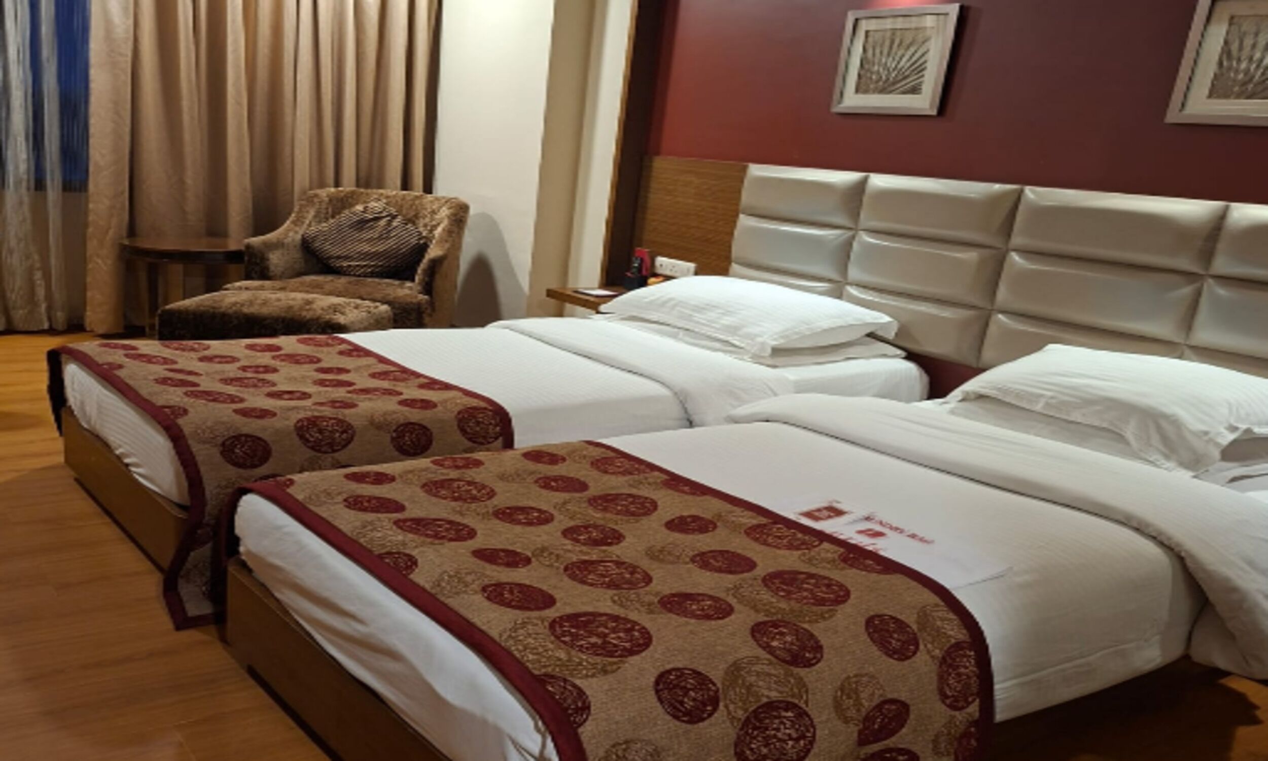 Habitación de hotel con dos camas, una silla, una mesita de noche y una pared con cuadros.